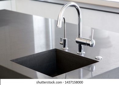 kitchen sink of dark gray stone with chrome faucet in a clean kitchen with a glossy work surface, close up faucet sink.