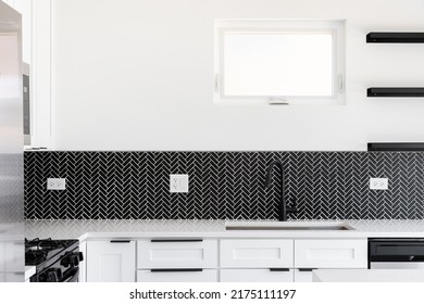 A Kitchen Sink Detail Shot With A Black Faucet, Black Marble Herringbone Backsplash, And A White Granite Countertop.