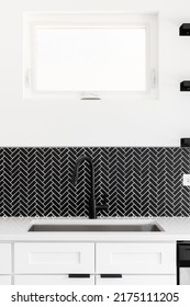 A Kitchen Sink Detail Shot With A Black Faucet, Black Marble Herringbone Backsplash, And A White Granite Countertop.