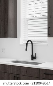 A Kitchen Sink Detail Shot With Dark Wooden Cabinets, A Black Faucet, And A White Marble Countertop And Backsplash In Front Of A Window.