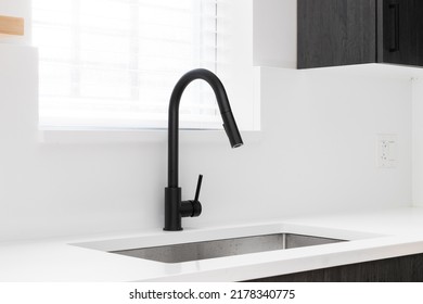 A Kitchen Sink Detail Shot With Dark Wooden Cabinets, A Black Faucet, And A White Marble Countertop And Backsplash In Front Of A Window.