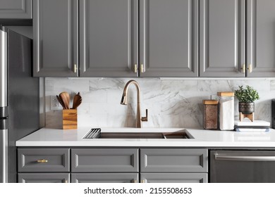 A kitchen sink detail shot with grey cabinets, a white marble countertop and backsplash, and decorations. - Shutterstock ID 2155508653