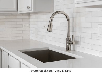 Kitchen sink detail shot with a marble subway tile backsplash, granite countertop, white cabinets, and a brushed gold faucet. - Powered by Shutterstock