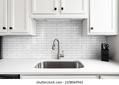 Kitchen sink detail shot with a subway tile backsplash, granite countertop, white cabinets, and a chrome faucet. - Shutterstock ID 2108069942