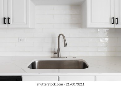 Kitchen Sink Detail Shot With A Subway Tile Backsplash, Granite Countertop, White Cabinets, And A Chrome Faucet.