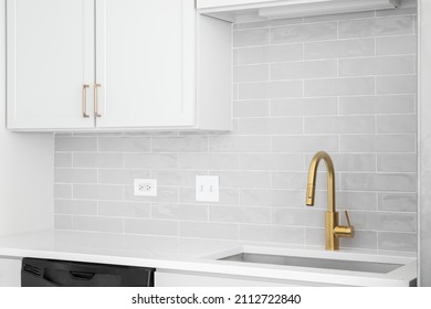 A Kitchen Sink Detail Shot In A White Kitchen With A Gold Faucet, Marble Countertop, And Grey Subway Tile Backsplash.