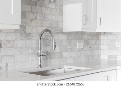 A Kitchen Sink Detail Shot With White Cabinets And A Marble Subway Tile Backsplash.