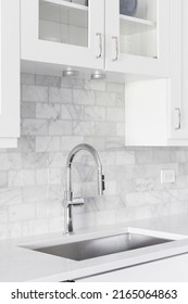 A Kitchen Sink Detail Shot With White Cabinets And A Marble Subway Tile Backsplash.