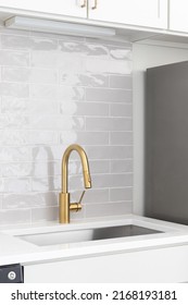 A Kitchen Sink Detail Shot In A White Kitchen With A Gold Faucet, Marble Countertop, And Grey Subway Tile Backsplash.