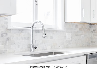 A Kitchen Sink Detail Shot With White Cabinets And A Marble Subway Tile Backsplash.