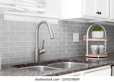 
A Kitchen Sink Detail Shot With White Cabinets, Grey Subway Tile Backsplash, And A Granite Countertop.