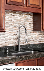 A Kitchen Sink Detail Shot With Wood Cabinets, A Tiled Backsplash, And Black Granite Countertop.