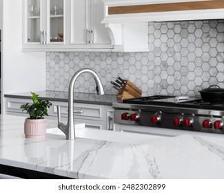 A kitchen sink detail, stainless faucet on a white farmhouse sink and marble counter, and a marble hexagon tiled backsplash with white cabinets. No brands or labels. - Powered by Shutterstock