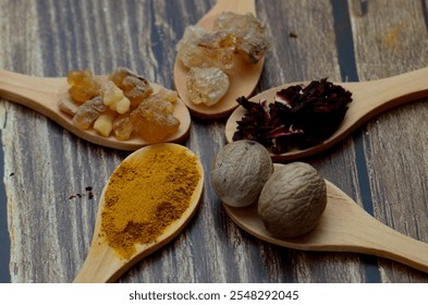 A kitchen studio food shot of various spices (Turmeric, Nutmeg, Hibiscus, Frankincense and Acacia) in a wooden spoons isolated on a wooden background.
