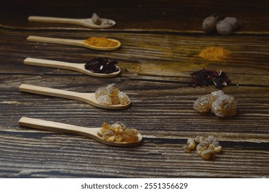 A kitchen studio food shot of various spices (Turmeric, Nutmeg, Hibiscus, Frankincense and Acacia) in a wooden spoons isolated on a wooden background.