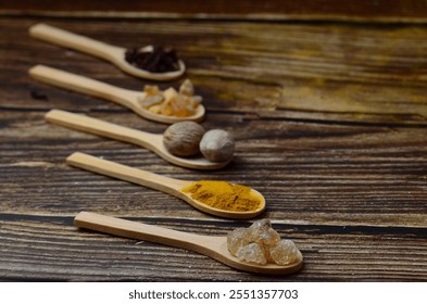 A kitchen studio food shot of various spices (Turmeric, Nutmeg, Hibiscus, Frankincense and Acacia) in a wooden spoons isolated on a wooden background.