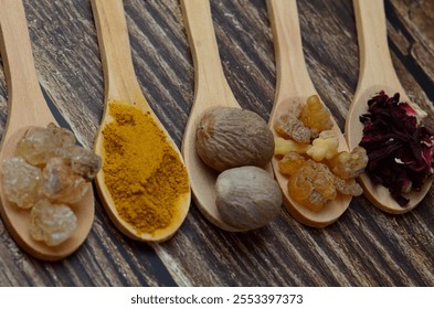 A kitchen studio food shot of various spices (Turmeric, Nutmeg, Hibiscus, Frankincense and Acacia) in a wooden spoons isolated on a wooden background. - Powered by Shutterstock