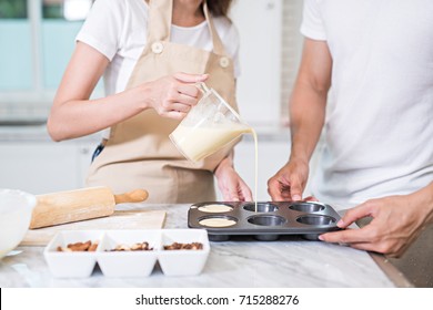 In The Kitchen, A Sweet Couple Pouring Cake Batter, The Mixed Of Flour, Milk, And Eggs  Into The Molds For Baking Cupcakes