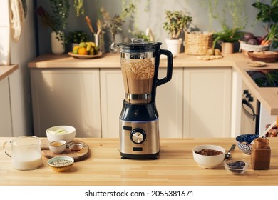 Kitchen table with electric blender with chocolate smoothie and bowls with ingredients
