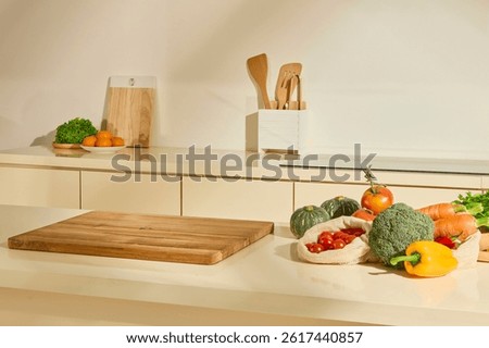 Kitchen table with empty wooden cutting board and vegetables such as cauliflower, bell pepper, cherry tomatoes, pumpkin, carrots. Wooden cutting board stands upright. Natural light floods the scene