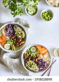 Kitchen table - two vegan tempeh poke bowls ready to be served for lunch. Bowls are full of rice, baked tempeh in hoisin sauce and fresh, colourful veggies. Healthy, delicious meal full of nutrients