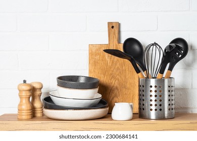 Kitchen table, kitchen utensils, plates, bowls, shakers and wooden cutting board.