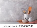 Kitchen table with white modern ceramic and wooden dishware against grey stone wall, baking utensils copy space