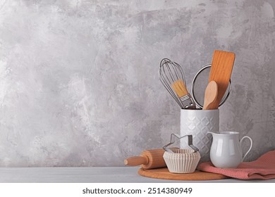 Kitchen table with white modern ceramic and wooden dishware against grey stone wall, baking utensils copy space - Powered by Shutterstock