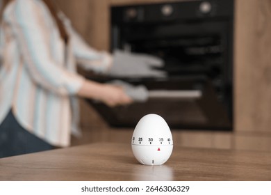 Kitchen timer on table against woman baking in room, closeup