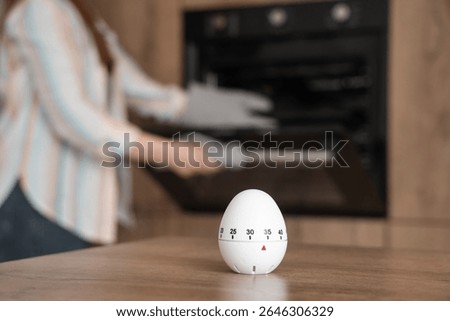 Kitchen timer on table against woman baking in room, closeup