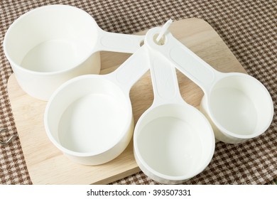 Kitchen Tools And Equipment, Four Plastic Measuring Cups In Different Sizes On Wooden Cutting Board.