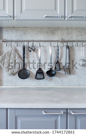 Kitchen tools on gray kitchen. Potholder, ladle, strainer, blade on railing at gray background.