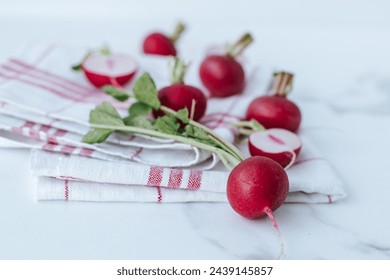 a kitchen towel with red stripes lies on a marble background, on it there are whole radishes and halves in a chaotic order - Powered by Shutterstock