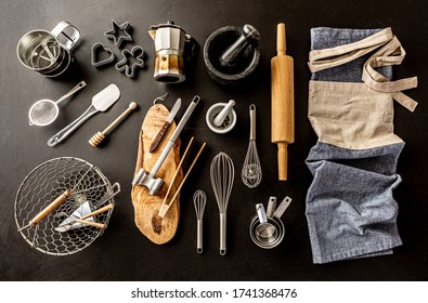 Kitchen Utensils (cooking Tools) And Chef’s Apron On Black Chalkboard Background. Kitchenware Collection Captured From Above (top View, Flat Lay).