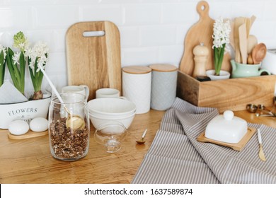 Kitchen utensils and dishware spring flowers on wooden table. Kitchen interior background white ceramic brick wall background. Eco friendly kitchen concept