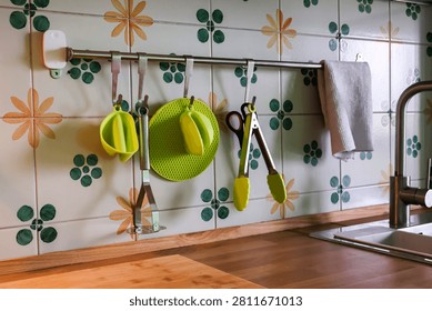 Kitchen utensils including scissors, masher, silicone accessories and cooking tools hanging on a metal rail in a modern home kitchen. Organization and cooking concept
