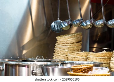 Kitchen Utensils In The Restaurant Kitchen. Soup Ladles Hang Over A Table With Pots And Wicker Plates. Kitchen Tools For Professional Chef.