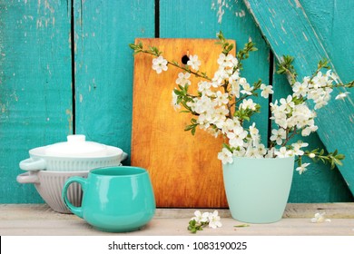 Kitchen ware set on bright turquoise wooden background, vintage crockery, chopping board and beautiful spring bouquet in a simple case, rustic design. Shabby chic