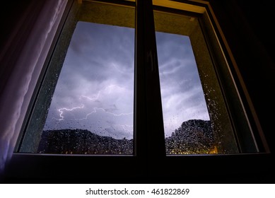 The Kitchen Window Lights Up During A Thunderstorm As Rain Splashes Against The Window.