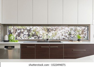 Kitchen Window with spring blossoms outside with black sink silver and brown timber cabinets with styled decor items on bench and dishwasher - Shutterstock ID 1522494071
