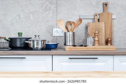 Mesa de madera de cocina con tabla de cortar de madera, picadora de especias y utensilios, encimera con sartenes en placa de inducción, cuchillos