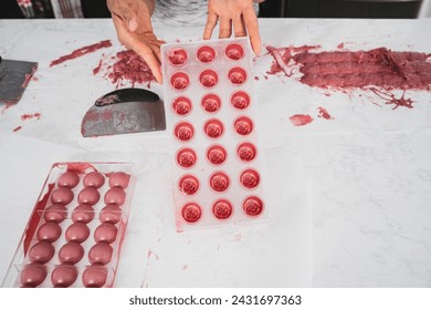 Kitchen work surface. Pink chocolate is poured into a plastic mold. Thickened chocolate spill. A woman holds in her hands a plastic mold filled with pink chocolate.

