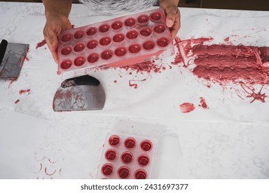 Kitchen work surface. Pink chocolate is poured into a plastic mold. Thickened chocolate spill. A woman holds in her hands a plastic mold filled with pink chocolate.

