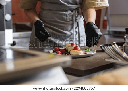 Kitchen worker decorated ready cheesecakes with berries for breakfast in restaurant