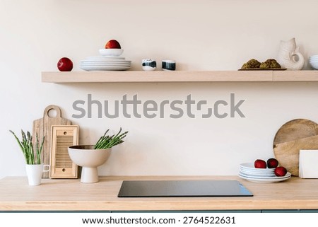 Kitchenware, dishware, home decor on countertop close to electric stove. Sleek induction hob and natural wooden counter in contemporary culinary environment. Interior design in modern house