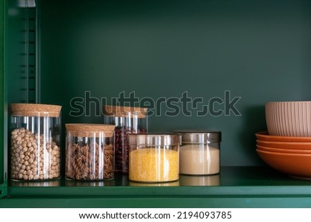 kitchenware, glass jars with beans, pasta and grains on metal green shelf at cabinet. storage food concept and order at kitchen