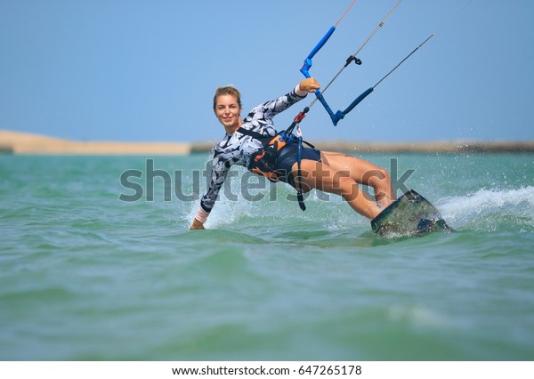 Kite surfing girl in sexy swimsuit with kite in sky\
on board in blue sea riding waves with water splash. Recreational\
activity, water sports, action, hobby and fun in summer time.\
Kiteboarding sport