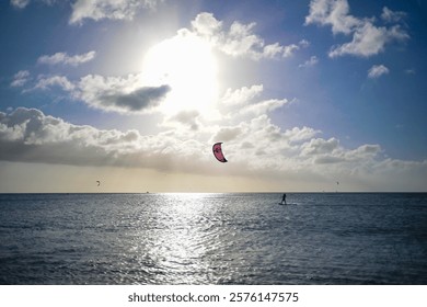 Kiteboarding under a bright sun with dramatic skies, showcasing the beauty of water sports and ocean adventures. Ideal for beach vacations and active lifestyle promotions. Stock photo 