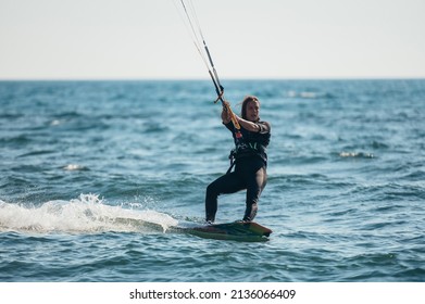 Kitesurfing woman in a wetsuit with kite in sky on kiteboard in blue sea riding waves with water splash. Water sports. Hobby and fun in summer time. Kiteboarding sport.