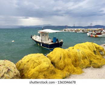 Kiveri, Argolis, Greece, 20 October 2018. Stormy Weather, Rough Sea, Fishing Boat Moored By Yello Fishing Nets. Green Water And Heavey Grey Sky With Thick Clouds.mountains Far Ahead. Light House.